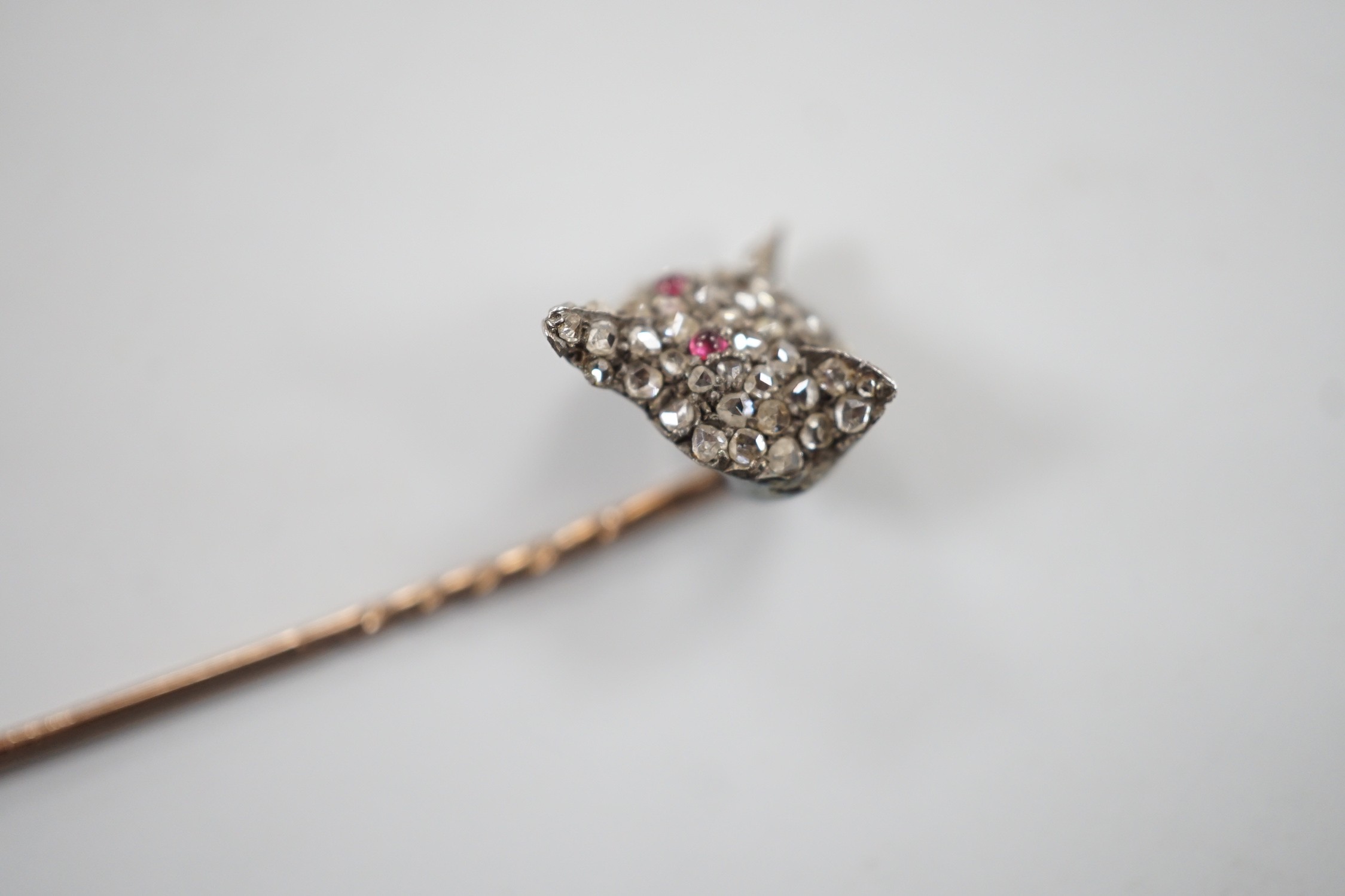 A late Victorian yellow and white metal, cabochon ruby? and rose cut diamond set fox head stick pin, 56mm, gross weight 4.7 grams (two stones missing).
